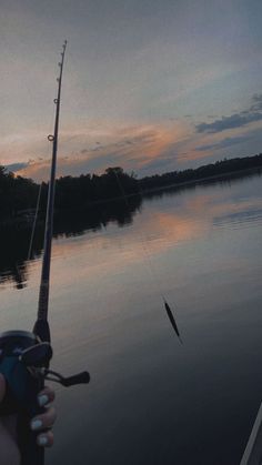 a person holding a fishing rod on the side of a river at sunset or dawn