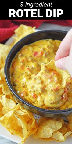 a hand dipping tortilla chips into a black bowl filled with cheese and salsa