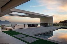 an outdoor living area with couches and tables near the water's edge at sunset