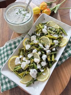 a white plate topped with asparagus and lemons next to a bowl of yogurt