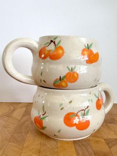 two white cups with oranges painted on them sitting on a wooden table next to each other