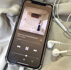 an iphone with headphones and music player on the screen next to earbuds