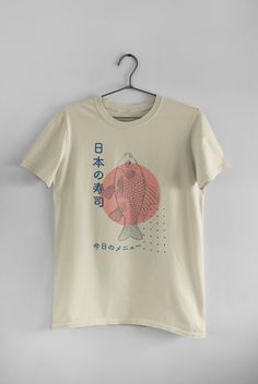 A simple and stylish graphic tee that features a fish and Japanese characters. A cute Japanese shirt that has a unique and stylish graphic design. A navy design with a pink accent on a cream t-shirt. Cheap Watercolor Print Graphic Tee, Japanese Shirts Women, Cheap Graphic Tee With Watercolor Print, Retro Character, Japanese Shirt, Japanese Fish, Shirt Logo Design, Japanese Tshirt