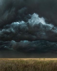 the sky is filled with dark clouds over an open field