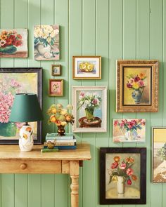 a room with green walls and pictures on the wall next to a wooden table topped with a lamp