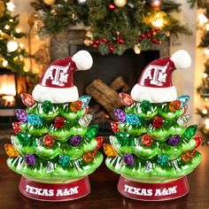 two glass christmas trees with hats on them sitting in front of a fireplace decorated for the holidays