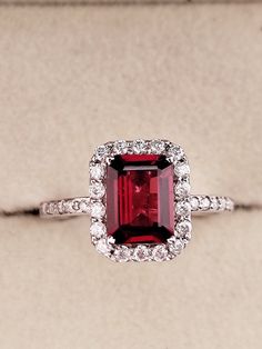 an engagement ring with a red stone surrounded by diamonds