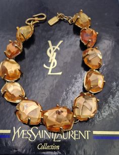 This vintage 90's resin necklace signed Yves Saint Laurent by Robert Goossens is superb.  It is made of champagne-colored resin and gold-plated metal.  Measurements: the necklace is 17,3 in long and is adjustable from 16,2 cm to 44 cm  YSLMade in France Metal Lobster Clasp with Logo Signed YSL made in France  Although it is important, it is light, its weight is 130 g  It is in excellent vintage condition, however I would like to point out that one of the resin pebbles shows signs of use (see the Designer Gold Necklaces, Designer Gold Necklaces For Evening, Formal Gold Lucite Jewelry, Yves Saint Laurent Logo, Saint Laurent Jewelry, Saint Laurent Logo, Logo Sign, Resin Necklace, Lobster Clasp