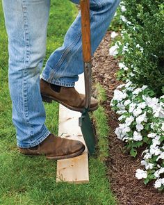 a man is using a garden tool to trim the grass in his front yard with white flowers