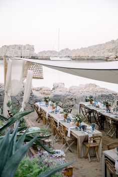 an outdoor dining area with tables and chairs set up for dinner on the beach next to water