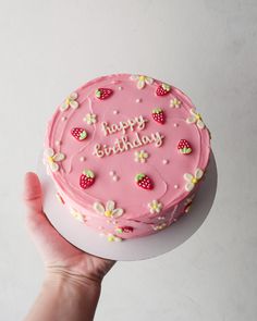 a pink birthday cake with strawberries and flowers on it is being held by a person