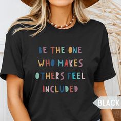 a woman wearing a black t - shirt that says be the one who makes others feel included