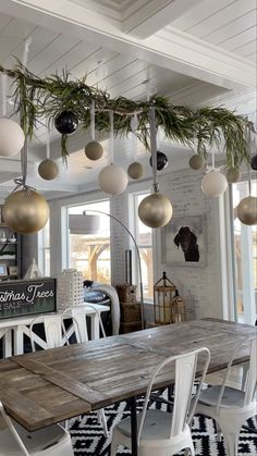 a dining room table with white chairs and hanging christmas ornaments on the ceiling above it