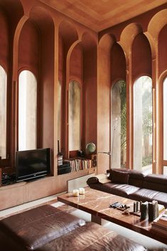 a living room filled with brown furniture and tall arched windows next to a flat screen tv