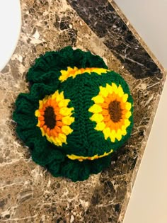 a green and yellow knitted hat with sunflowers on the top sitting on a marble counter