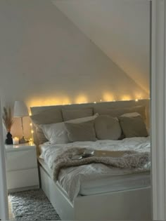 a white bed sitting in a bedroom next to a night stand with lights on it