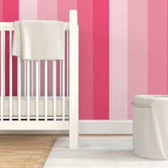 a white crib in front of a pink and red striped wall with a trash can