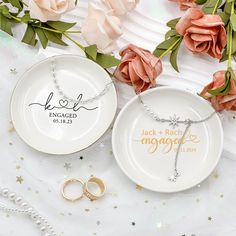 two personalized wedding rings and ring dish on a white tablecloth with pink roses