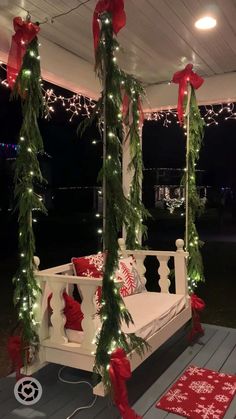 a porch swing covered in christmas lights and greenery with red bows on the posts