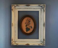 a white frame holding a painting with flowers on it in a blue walled wall area