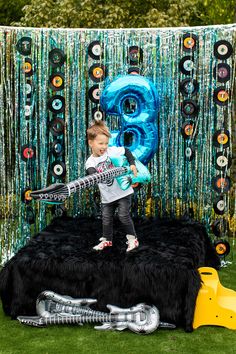 a young boy standing on top of a black table covered in fake furs and balloons