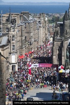 a large group of people walking down a street next to tall buildings with flags on them