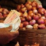 a person holding money in front of baskets filled with onions