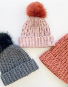 three knitted hats with pom - poms on them sitting next to each other