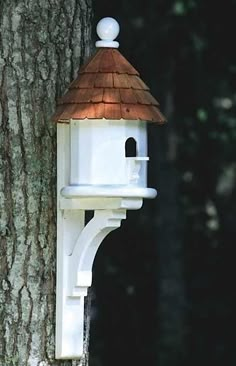 a bird house attached to the side of a tree in front of a large tree