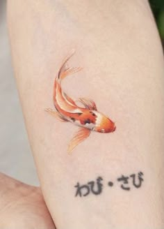 a goldfish tattoo on the left arm with words written below it in cursive writing