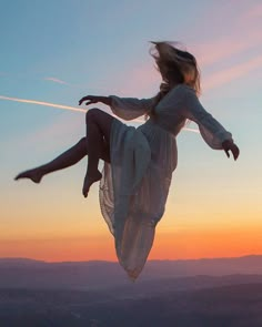 a woman flying through the air while wearing a white dress in front of a sunset