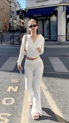 a woman walking down the street wearing white pants and a cropped top with cutouts