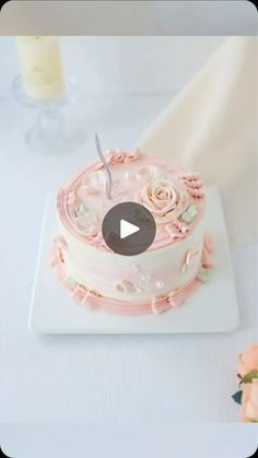 a cake with pink frosting and flowers is on a white plate next to a candle