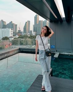 a woman in white shirt and jeans standing on top of a building next to water