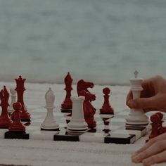 someone playing chess on the beach with their hand over the white board and red pieces