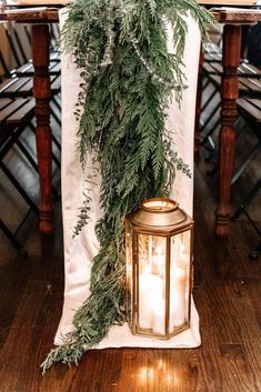 a candle is lit next to a table with greenery on it and an old fashioned lantern