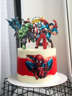 a birthday cake decorated with the avengers and spider - man characters on top is sitting on a wire rack