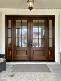 the front door of a house with two large brown doors and one light on it's side