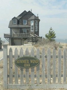 a wooden fence with a sign that says summer wind on it and a house in the background