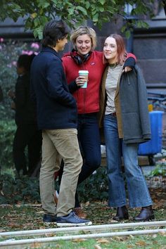 two women and a man standing next to each other in front of a tree with their arms around one another