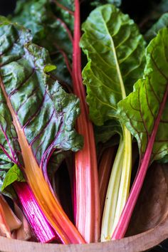 a wooden bowl filled with lots of green leafy vegetables