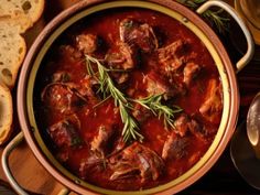 meat stew in a pot with bread on the side and wine glasses next to it