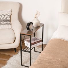 a white chair sitting next to a table on top of a hard wood floor near a bed