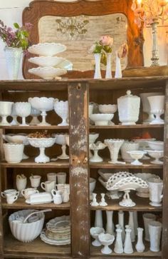 a wooden cabinet filled with lots of white dishes and vases on top of it