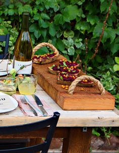 the table is set with food and wine for two people to enjoy in the garden