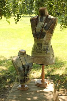 two mannequins with necklaces on display under a tree in a park