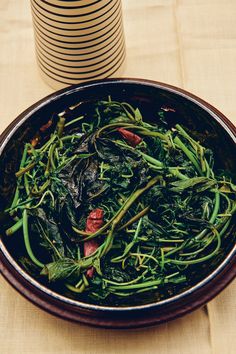 a bowl filled with green vegetables on top of a table next to stacks of plates