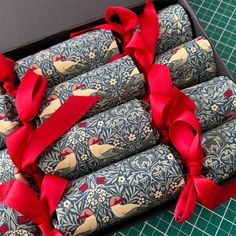 four wrapped crackers in a box with red ribbon around them on a green table