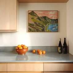 a bowl of oranges sitting on top of a kitchen counter next to bottles of wine