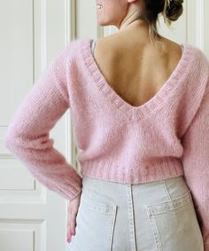 a woman wearing a pink sweater and white pants with her back turned to the camera